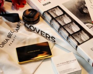  A review of the latest makeup launch from this former Spice girl. It's clean beauty, it's sustainable and it's gorgeous! In this image the eyeshadow palette and glitter eyeshadow are closed and sit on a makeup bag with the VB logo with photography books in the background.