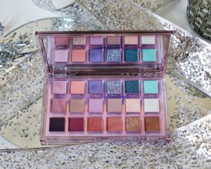 Huda Beauty Mercury Retrograde eyeshadow palette! A glitter and shimmer eyeshadow palette to create christmas, xmas and party makeup looks. It sits on a mirrored surface surrounded by sequins.