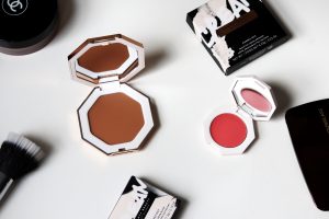 Fenty cream bronzer and blushers are laid with their boxes on a white table.