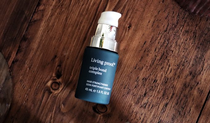 Living Proof Triple Bond Complex Hair treatment. A blue bottle of hair serum is laid flat on a wooden table. Beauty blogger Amy reviews this today.