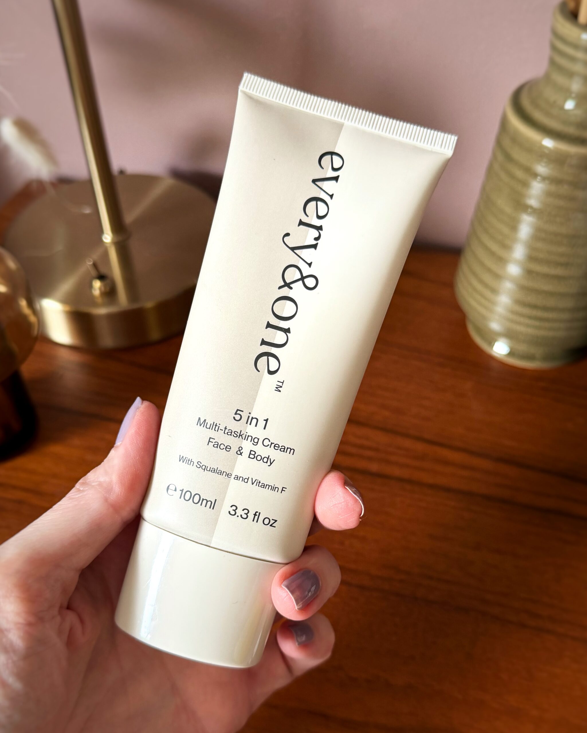 Amy is holding the cream and beige modern pack of cream. It is 100ml and has black text
